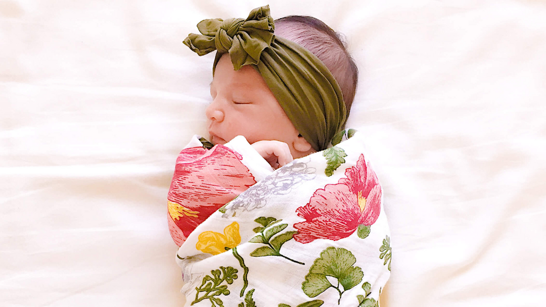 A sleeping baby girl wrapped in a floral bamboo blanket