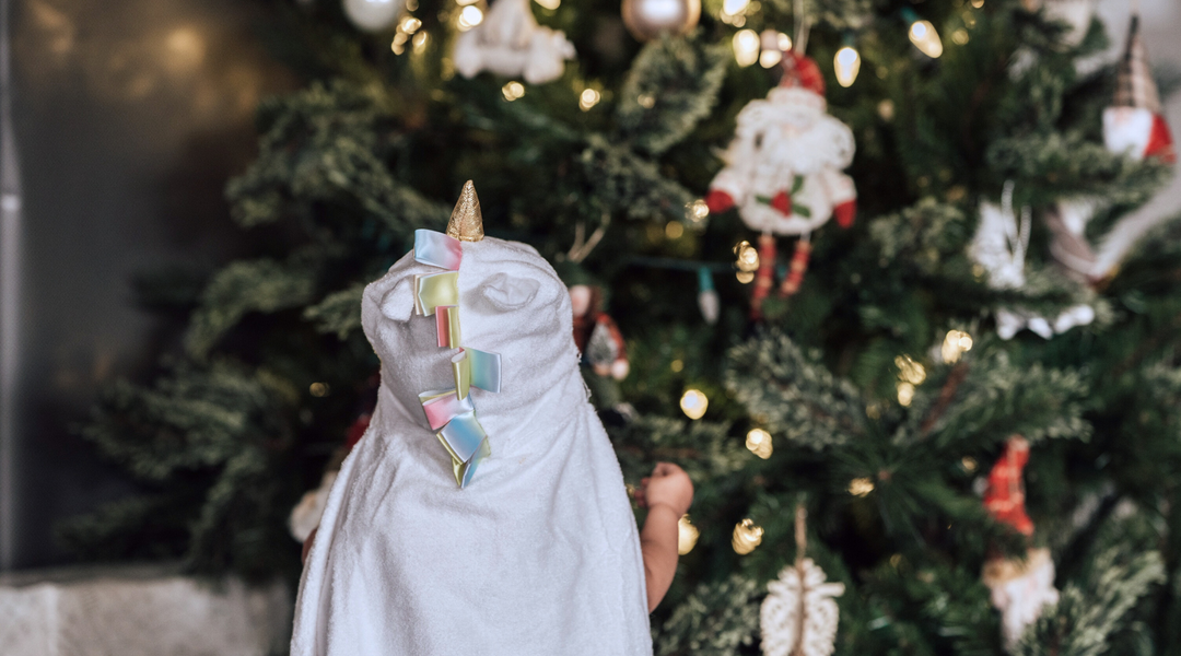 a child wrapped in kloud bambu white unicorn hooded towel standing in front of a christmas tree