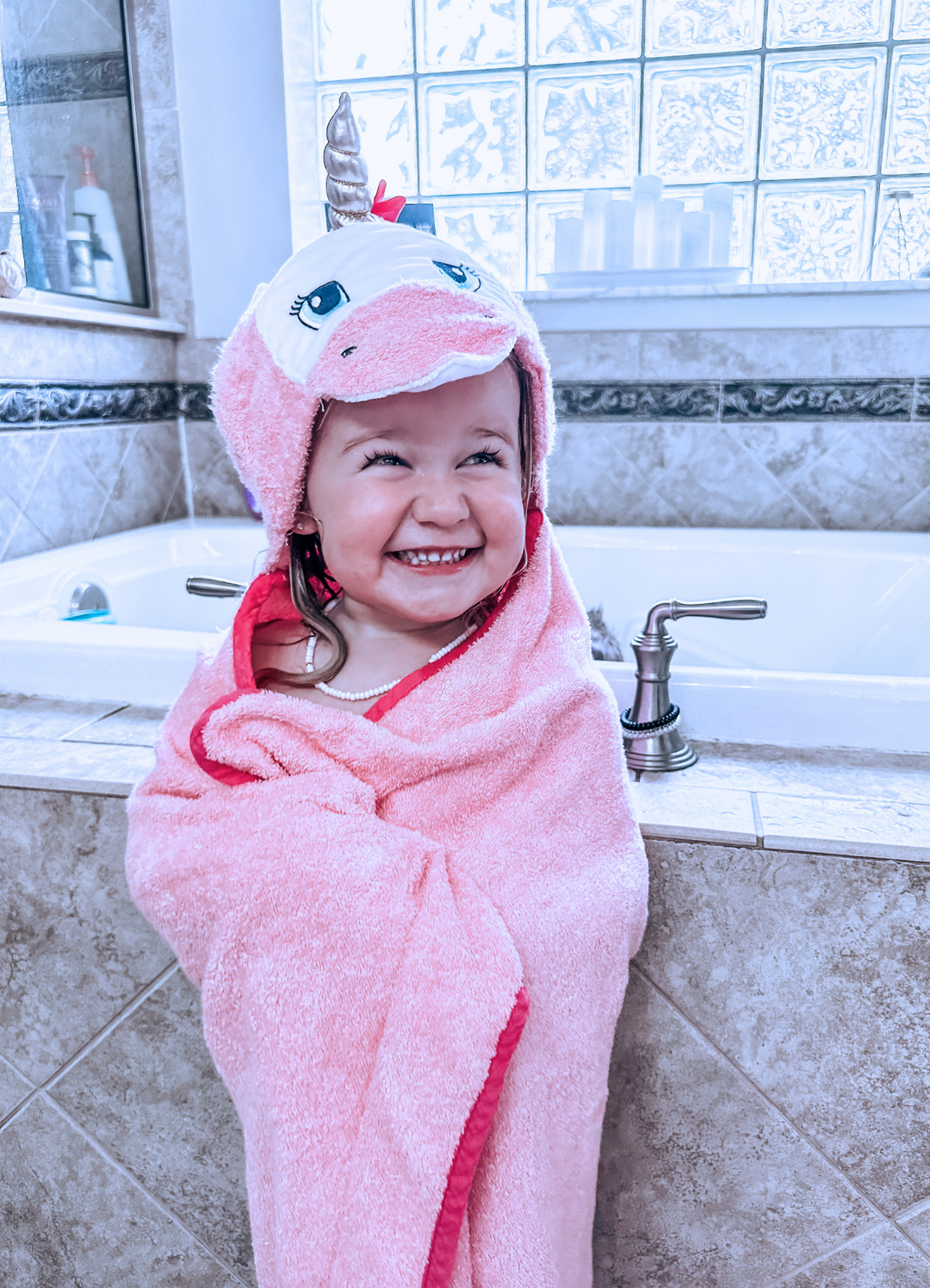 a girl child wrapped in kloud bambu pink unicorn hooded towel while standing beside the bath tub
