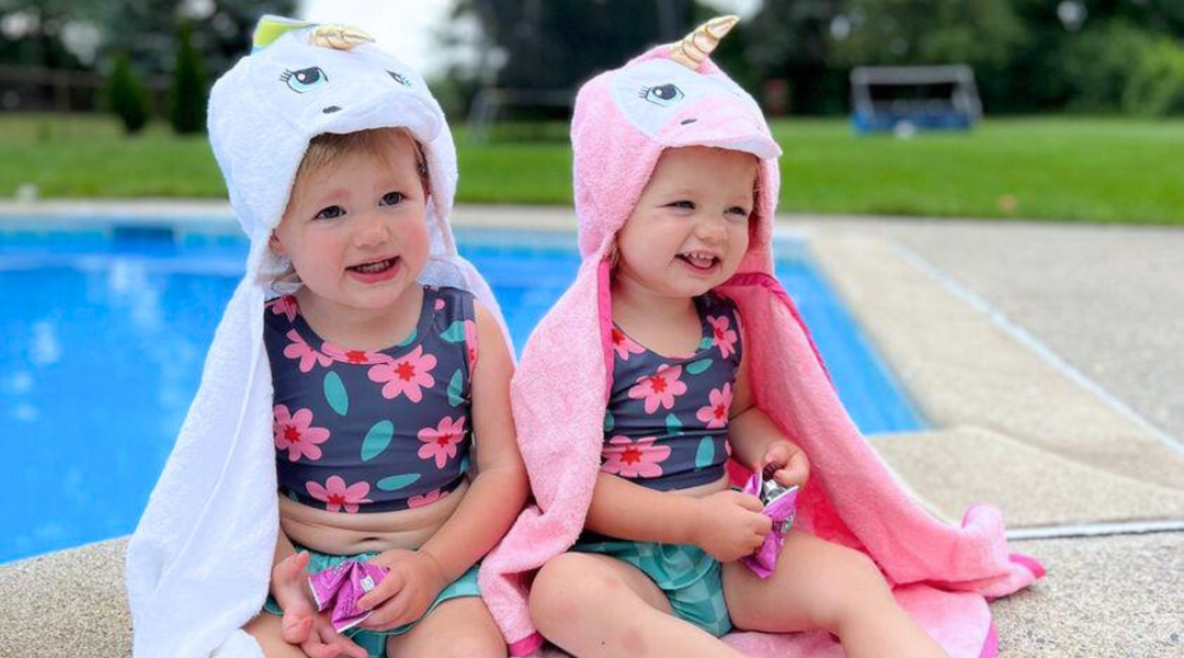 twin girls sitting by the pool wearing the kloud bambu white and pink unicorn bamboo baby hooded bath towels