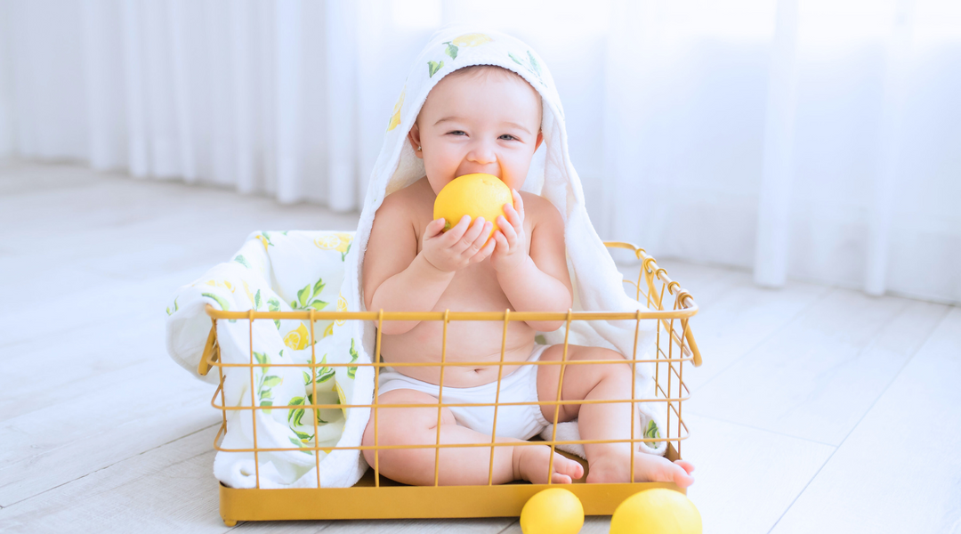 a baby holding a lemon while sitting on a basket with a lemon towel at the back